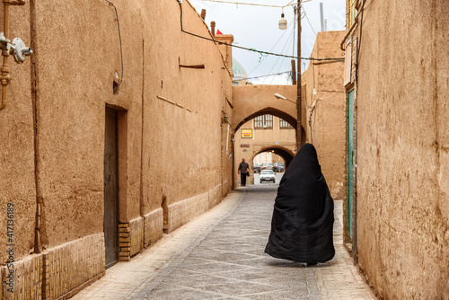 Foto Iranian woman wearing black chador walking along street of Yazd