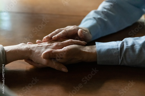 Senior adult husband consoling middle aged wife, expressing love, tender care, giving support. 60s pensioner couple hold hands at romantic or difficult moment. Close up of arms. Health therapy concept