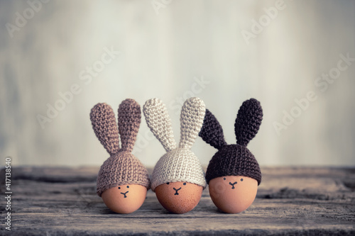 Three Easter eggs in crochet hats with bunny ears on old wooden table.