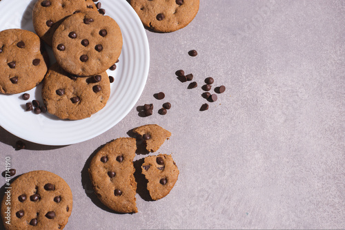Homemade chocolate chip cookies on a small plate with gray background, top view. Hard and contrasting shadows