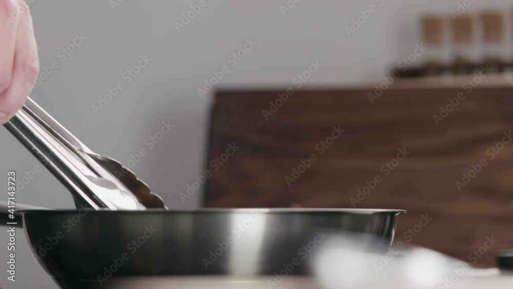 Slow motion shot of cooking steak on nonstick pan with tongs