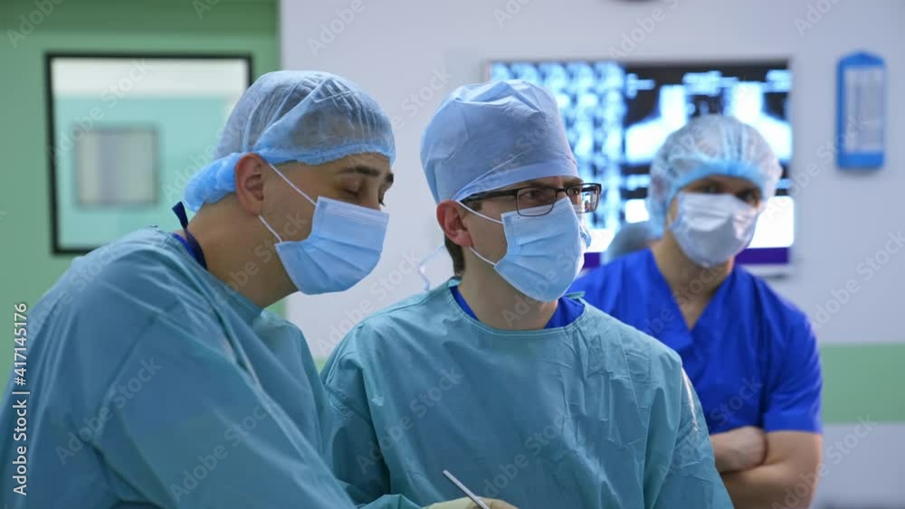 Male surgeons work together. Medical specialists perform a surgery and observe the process on monitor in the operating room. Male surgeons work together. Medical specialists perform a surgery and observe the process on monitor in the operating room.