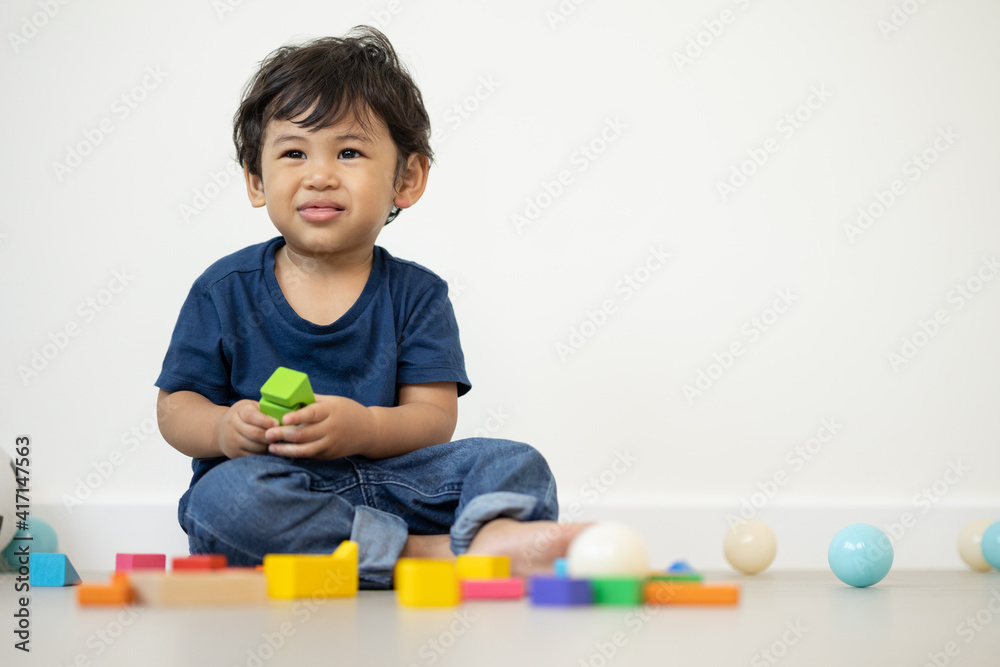 An Asian boy about 1 year old. Playing in the living room in the house He plays wooden toys in different colors. He is wearing a blue shirt.