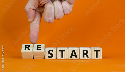 Start or restart symbol. Businessman turns wooden cubes and changes the word 'start' to 'restart'. Beautiful wooden table, orange background. Business, start or restart concept. Copy space.