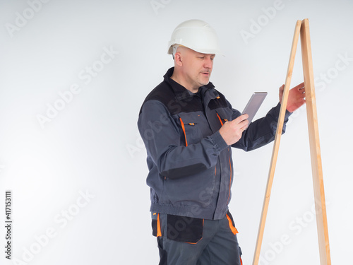 Builder or carpenter with a telephone. Carpenter on a white background. Portrait of engineer in uniform and helmet. Builder is holding timber beams. Concept carpenter looking at something on internet