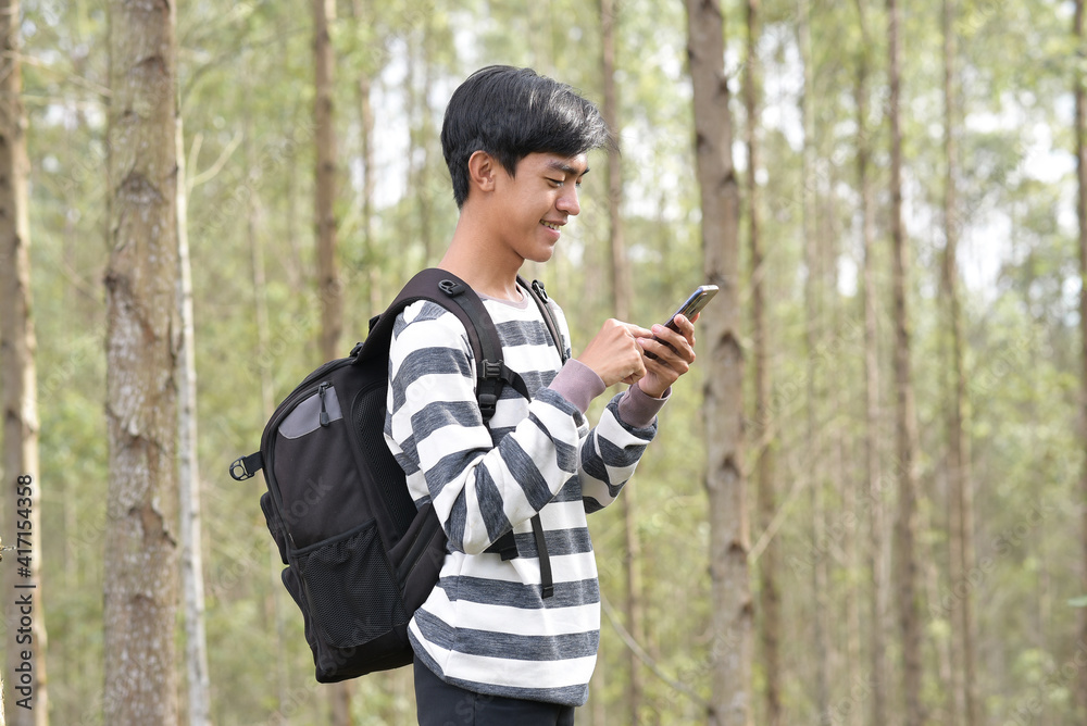 Asian man using smartphone in nature with backpack Asian man using smartphone in nature with backpack