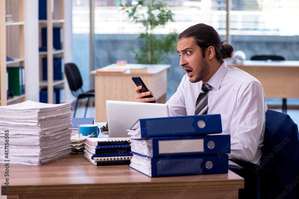 Young male employee unhappy with excessive work in the office Young male employee unhappy with excessive work in the office