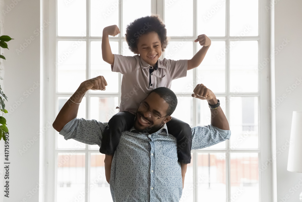 © fizkes - Happy funny kid riding on dads shoulders. African American daddy wearing glasses and son playing together, showing hand strength, flexing biceps, laughing and having fun. Family home activity concept © fizkes - Happy funny kid riding on dads shoulders. African American daddy wearing glasses and son playing together, showing hand strength, flexing biceps, laughing and having fun. Family home activity concept
