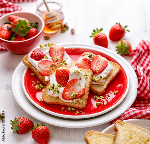 Delicious homemade toasts with fresh strawberries and cream cheese sprinkled with pine nuts, close-up view.
