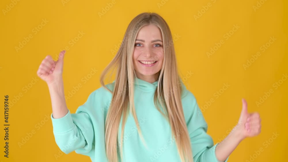Positive young girl posing isolated on yellow studio background. Woman Looking approvingly at camera showing thumbs up, like sign positive something good. People lifestyle concept. Positive young girl posing isolated on yellow studio background. Woman Looking approvingly at camera showing thumbs up, like sign positive something good. People lifestyle concept.