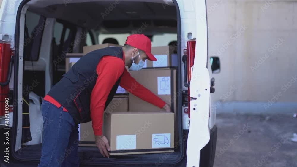 Delivery man taking packages out of truck while wearing safety mask for coronavirus prevention Delivery man taking packages out of truck while wearing safety mask for coronavirus prevention
