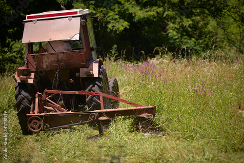 an old red tractor mowing the grass near the forest. use of agricultural machinery on the farm