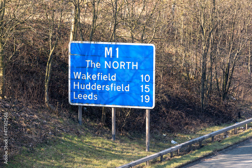 Slightly dirty road sign on the M1 motorway advising drivers of how many miles remain between that point and Wakefield, Huddersfield and Leeds