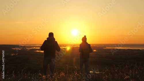 Carefree tourists travel at sunset. Teamwork in business. Free travelers  a man and woman with backpacks  descend from mountain in rays of dawn  enjoy nature  beautiful sun and landscape.