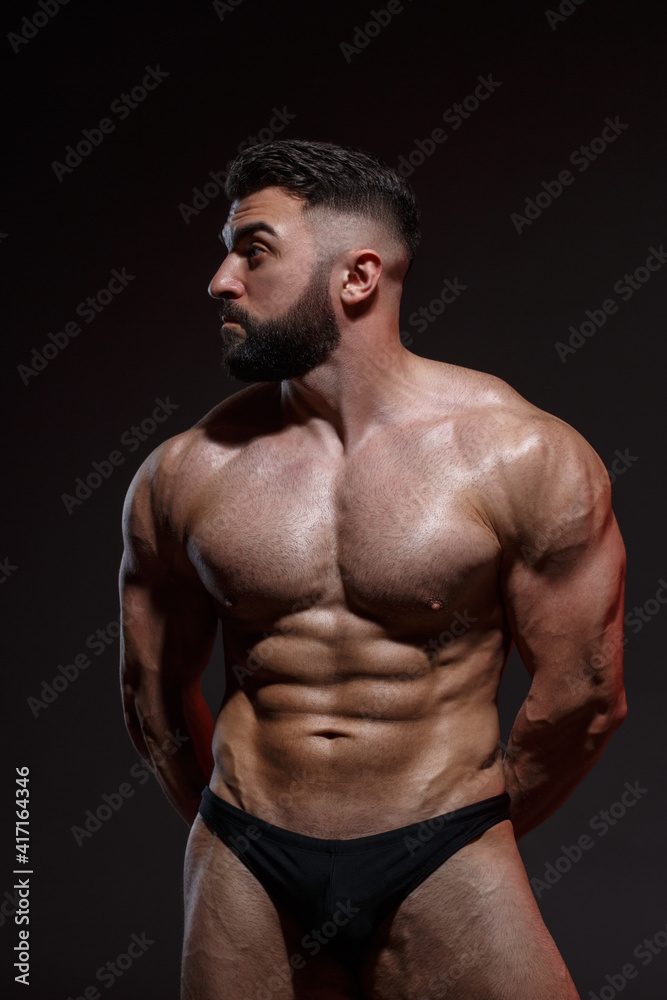 Young athletic male athlete with a beard shows muscles isolated on a dark background.