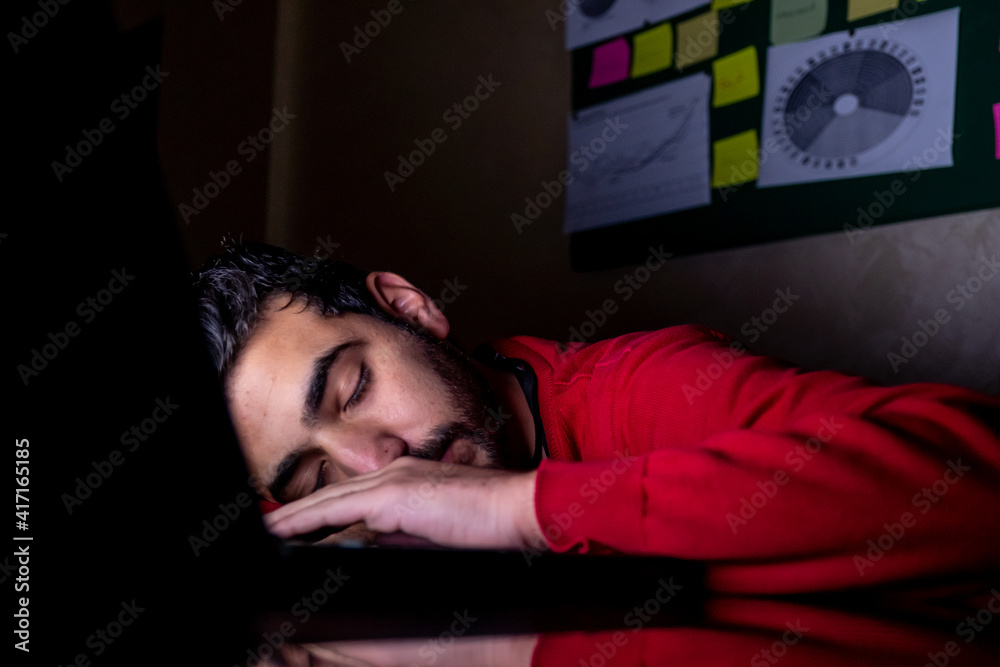 Young man is sleeping in his dark office after long term of working and overtime in front of his laptop Young man is sleeping in his dark office after long term of working and overtime in front of his laptop