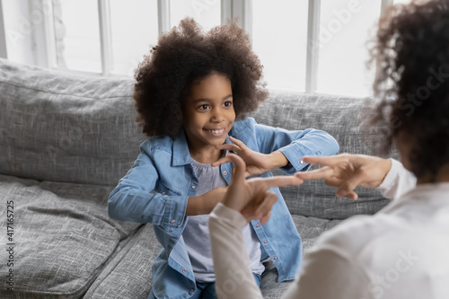 Happy girl talks to disabled deaf mom. Mother teaches kid sign language, shows hand gestures and finger symbols. Tutor giving lesson to positive child with hearing disability at home. Children therapy photo