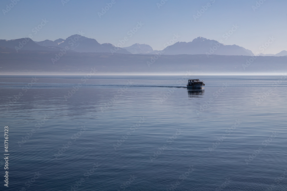A boat on hazy, misty Lake Geneva and the Alps seen from Lausanne, Switzerland