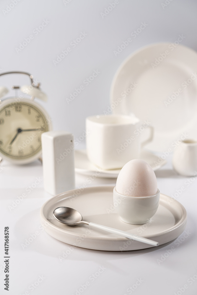 White egg with white plates, cup and alarm clock over white background for breakfast White egg with white plates, cup and alarm clock over white background for breakfast