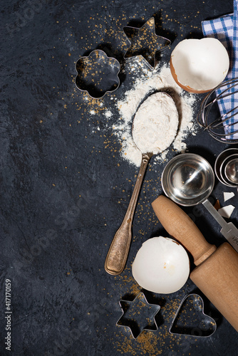 spoon with flour, forms and ingredients for baking on a black background, vertical