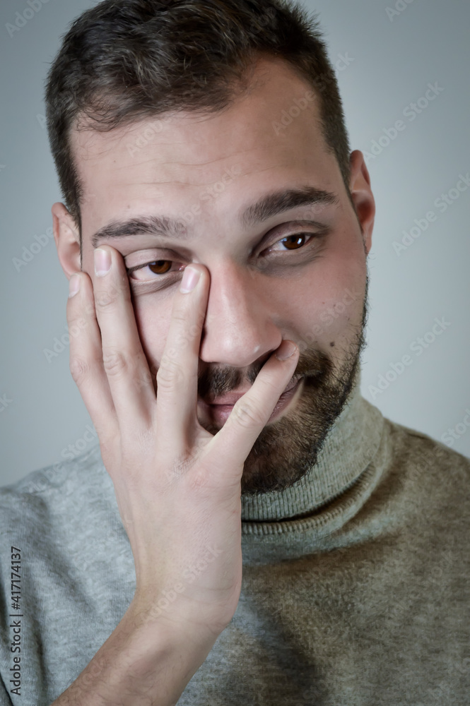 Portrait of a smiling young man covers his face with an ironic and fondling look
