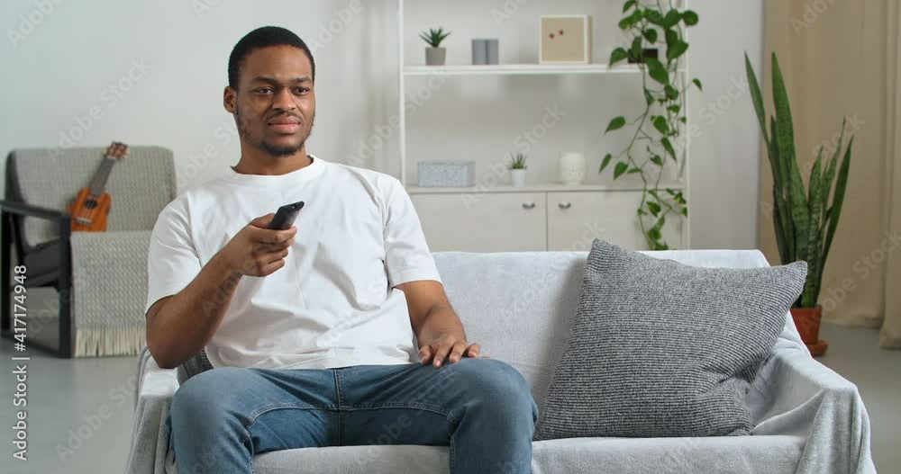 Afro american guy fan emotional bachelor wears casual clothes at home sitting in modern living room cheering for his favorite team watching tv online broadcasting sports game happy to win success