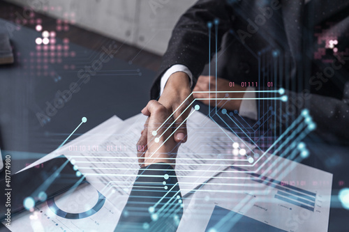 Handshake of two businesswomen who enters into the contract to develop a new software to improve business service at a company. Technological icons over the table with the document.