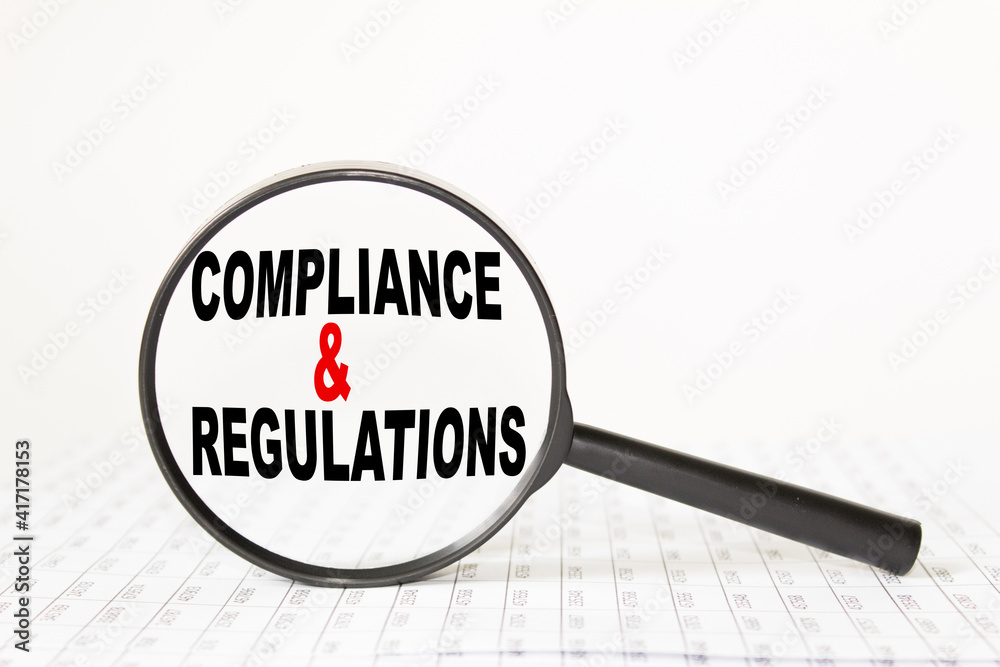 words COMPLIANCE AND REGULATIONS in a magnifying glass on a white background. business concept words COMPLIANCE AND REGULATIONS in a magnifying glass on a white background. business concept