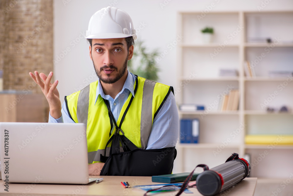 Young arm injured male architect working in the office Young arm injured male architect working in the office