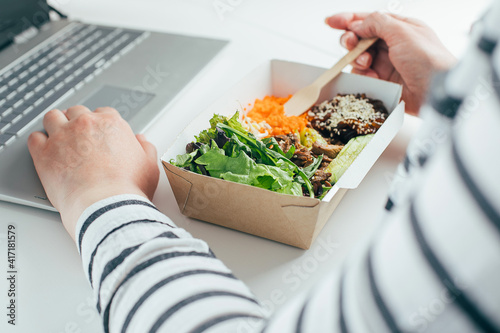 Woman having lunch in recycled bowl using laptop. Food delivery, quarantine, take out food concept