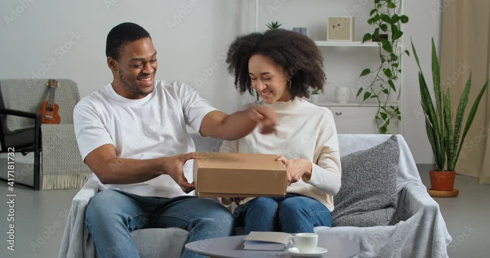 Afro american couple black husband and wife consumers buyers receive parcel by mail from internet store with interest open cardboard box feel surprise delight in gift of product, delivery concept Afro american couple black husband and wife consumers buyers receive parcel by mail from internet store with interest open cardboard box feel surprise delight in gift of product, delivery concept
