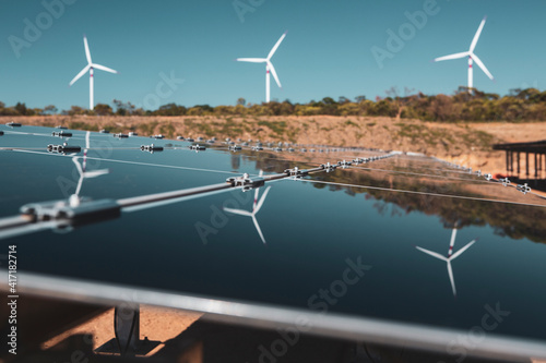 Solar panels under a beautiful blue sky reflecting windmills of an eolic windfarm. Renewable energy generation for environmental conservation concept. 