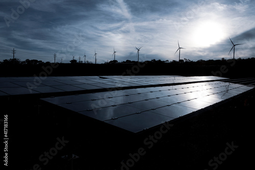 Wind farm and solar panels under a beautiful white sunset among the clouds. Renewable energy generation for environmental conservation concept. 