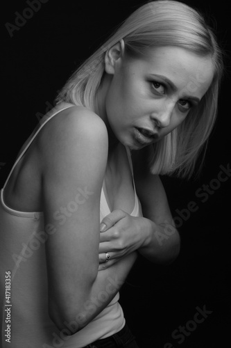 black-and-white portrait of a blonde on a black background. in a white tank top with straps © Roman Kornev