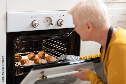 Over shoulder shot of senior woman checking croissants in oven