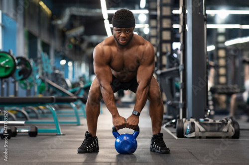 Muscular shirtless black man bodybuilder exercising with kettlebell at gym