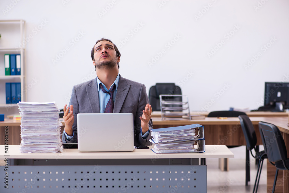 Young male employee unhappy with excessive work in the office Young male employee unhappy with excessive work in the office