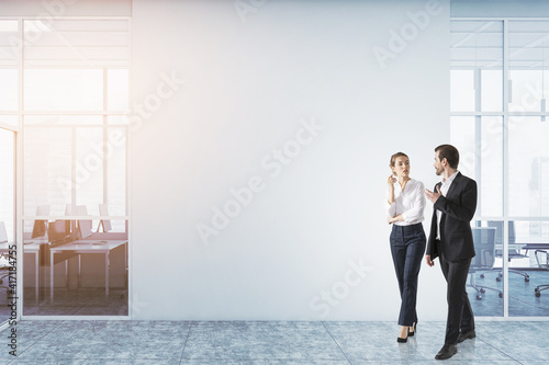 Handsome businessman and attractive businesswoman in formal wear chatting and walking along office space with panoramic windows. Mockup. Concept of success in career. photo