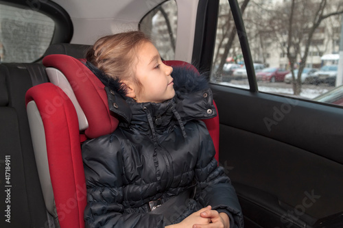 girl in blue warm clothes sits unbuckled in car seat photo