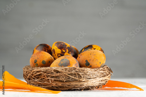 Easter quail eggs in a nest and orange feathers on a wooden table on a gray background. Easter holiday concept. Close up, copy space