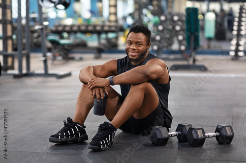 Smiling black muscular man having break while exercising at gym