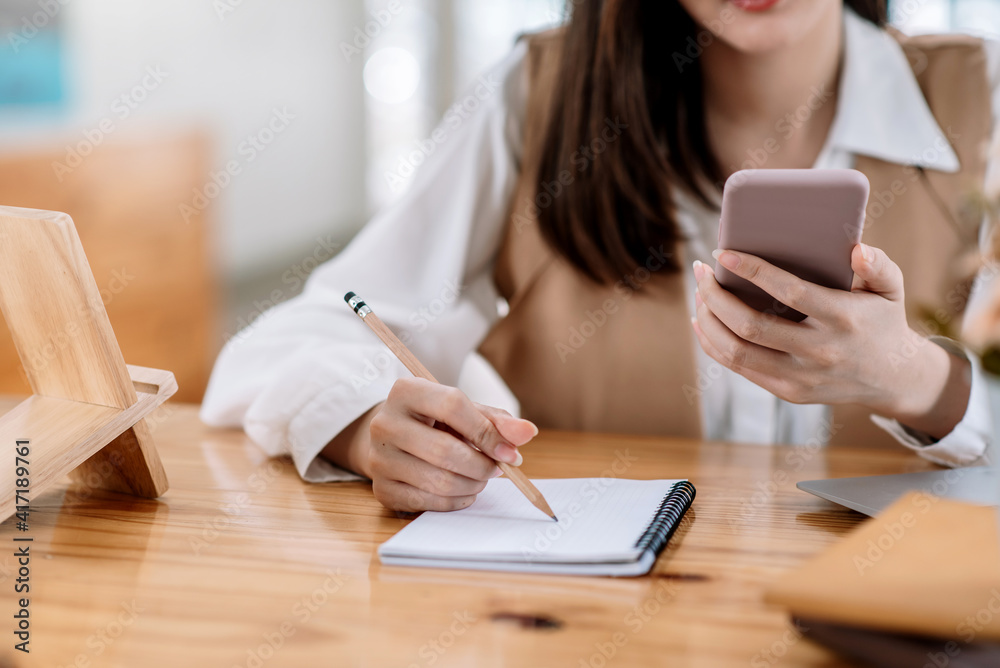 Close up of a woman hand using mobile phone and taking notes at the office. Close up of a woman hand using mobile phone and taking notes at the office.