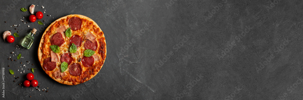 Fototapeta Fresh pepperoni pizza on a concrete table with cooking ingredients cherry tomatoes, basil and olive oil. Banner. Top view.