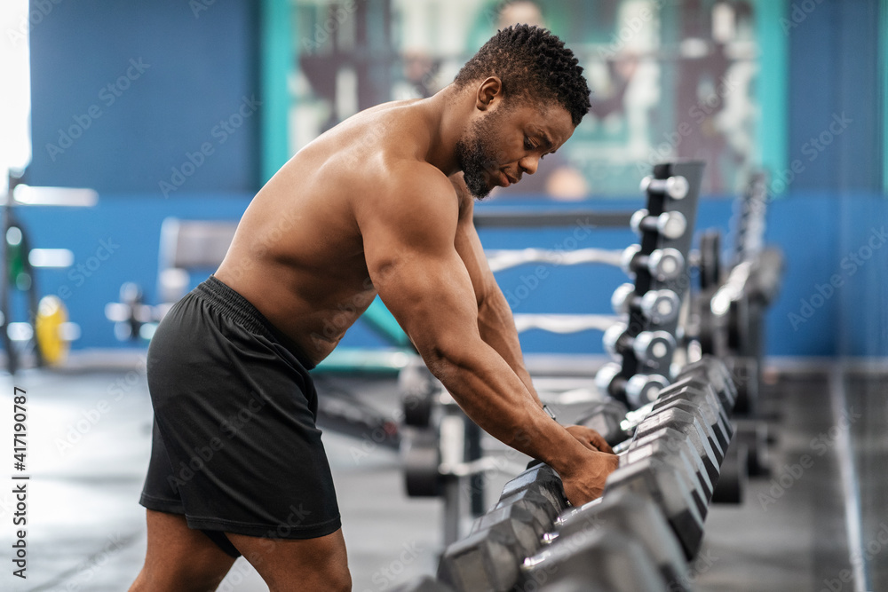 Shirtless african american bodybuilder grabbing dumbbell in gym Shirtless african american bodybuilder grabbing dumbbell in gym