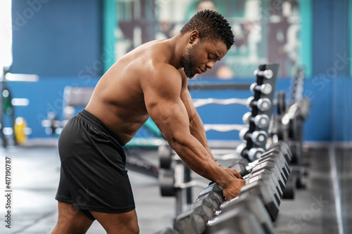 Shirtless african american bodybuilder grabbing dumbbell in gym