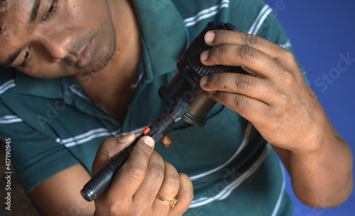 An Indian man technician inspecting and cleaning dslr or mirrorless camera lens. © Somnath
