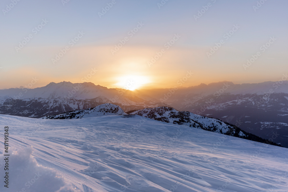 The sunset in winter during a wind storm with the snow being blown away on a peak near Lenzerheide in Switzerland