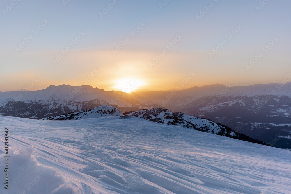 The sunset in winter during a wind storm with the snow being blown away on a peak near Lenzerheide in Switzerland