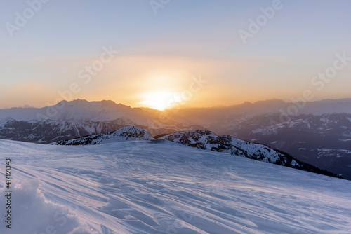 The sunset in winter during a wind storm with the snow being blown away on a peak near Lenzerheide in Switzerland