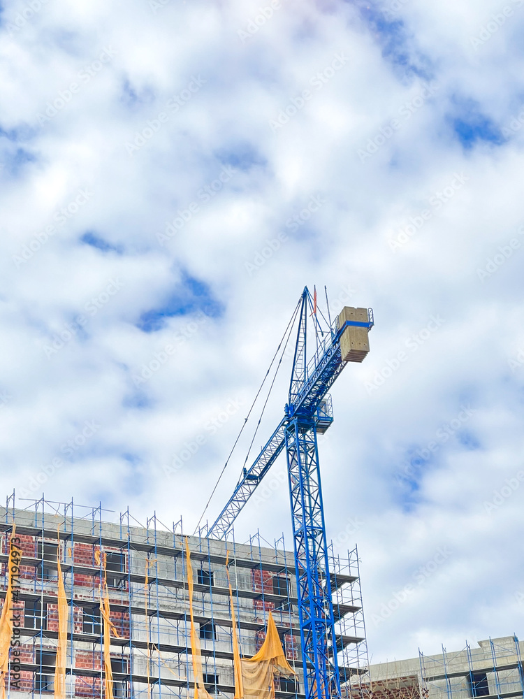 Large crane on a house construction, blue sky background.